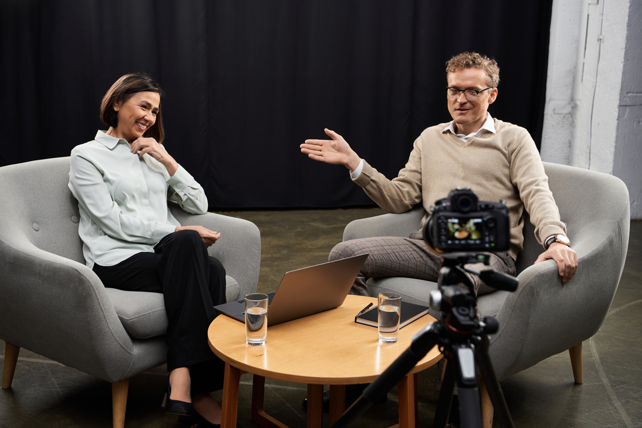 A female journalist interviews a male subject in a studio with a single camera setup.